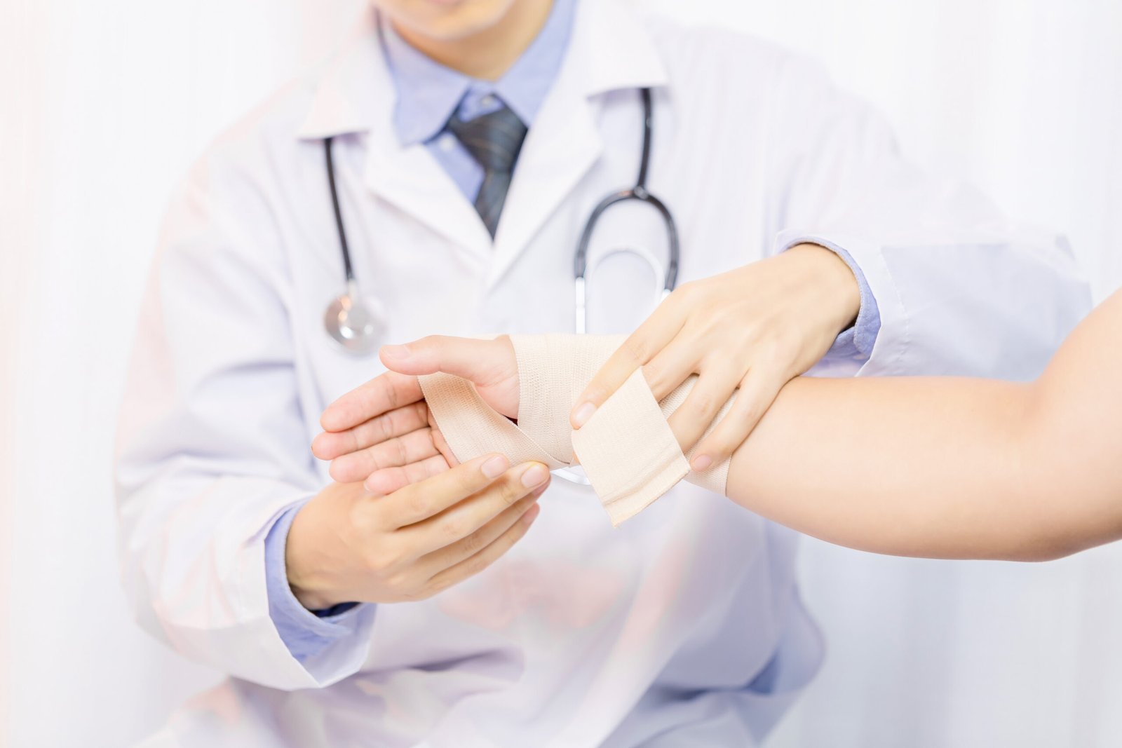 Male doctor putting gauze on young man's hand in clinic, closeup